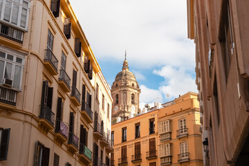 Obraz premium Low angle view of the majestic Malaga Cathedral bell tower rising above narrow residential streets with balconies, capturing the historic charm of the old town district in sunny Andalusia, Spain.