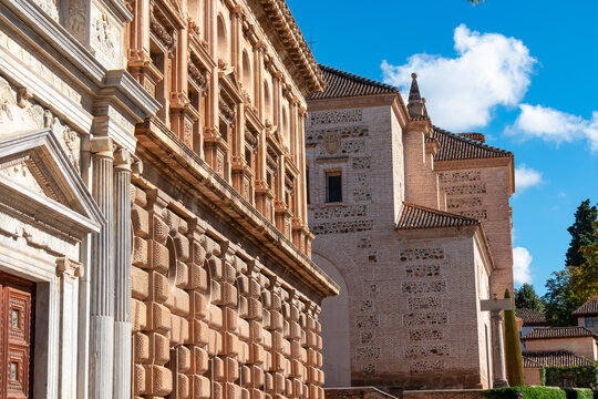 The rusticated stone wall of the Palace of Charles V stands beside the brick facade of the Santa Maria church in the Alhambra. architectural contrast highlights the rich history of Granada, Spain.
