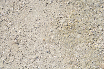 A top down view of a rough ground surface covered with small beige stones and dry dirt under bright...