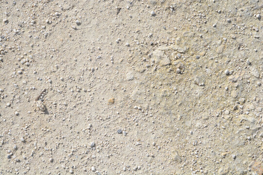A top down view of a rough ground surface covered with small beige stones and dry dirt under bright sunlight