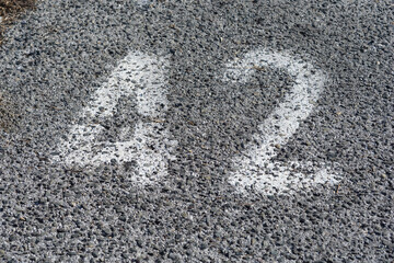 The number forty two is painted in white on a dark grey rough asphalt surface of a parking space or...