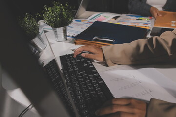 business documents on office table with tablet, smart phone and laptop and two colleagues discussing data