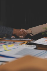 Entrepreneurs collaboration deal shaking hands in a modern office and financial paper graph on desk.