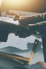 Entrepreneurs collaboration deal shaking hands in a modern office and financial paper graph on desk.