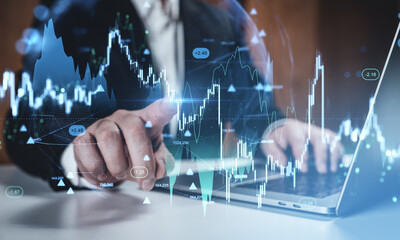 Businessman using laptop and touching digital forex chart with glowing hologram data on futuristic interface background representing financial trade concept.