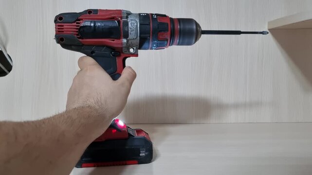 Right side profile view of a hand pressing the trigger of a red cordless drill to run the motor with a bit attached