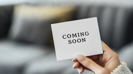 A hand holds a white card with "Coming Soon" printed in bold black letters, hinting at an upcoming announcement against a blurred background. Excitement builds for what's next!