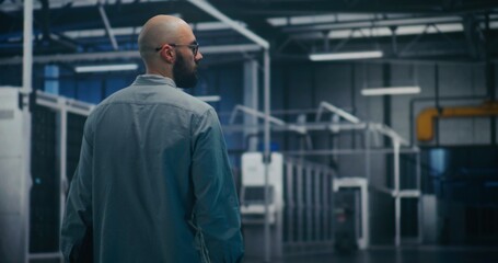 Engineer Inspecting Data Center Hall. Male IT Specialist Walks Through Massive Server or Industrial Hall. Emphasizes Facility Inspection, Professional Walking, and Scale of Infrastructure. Back View.