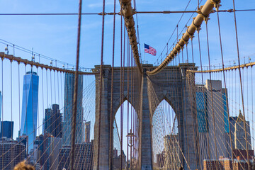 Obraz premium View through Brooklyn Bridge cables toward the Manhattan skyline and One World Trade Center with the American flag on the tower.