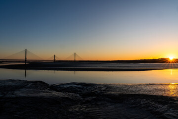 Obraz premium Mersey Gateway Bridge spanning the River Mersey at sunrise with exposed mudflats at low tide