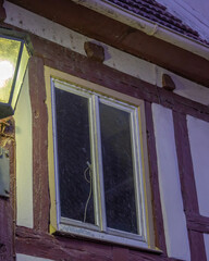 Old house with wooden beams, illuminated by street light at twilight, showcasing a window with a visible white cord
