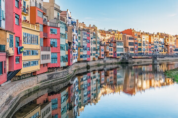 Colorful houses of Girona reflected in calm waters of Onyar River during golden hour, Spain....