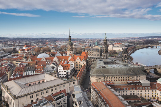 Dresden old town cityscape showcasing historic architecture, including the hofkirche and semperoper, with the elbe river flowing through the urban landscape under a partly cloudy sky