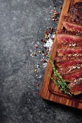 Grilled beef steak slices on a rustic wooden board, seasoned with sea salt, pepper, and fresh thyme herbs, ready to serve on a dark table