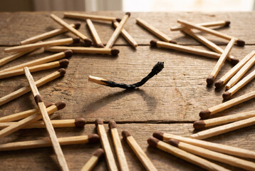 Burned matchstick surrounded by unused matches on wooden table, burnout, stress and mental exhaustion concept.