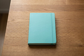 Fototapeta premium Closed turquoise notebook on wooden desk, minimal stationery mockup for journaling, planning and branding designs.