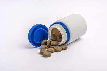 Brown herbal pills spilling out of a white plastic bottle on white background.