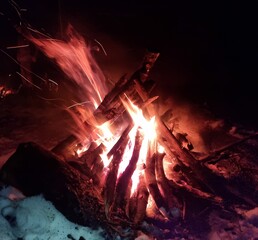 Night campfire in a winter forest. Flames and glowing embers on snow create a contrast of warmth and cold, symbolizing survival, nature connection, and calm during a winter adventure.