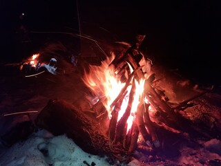 Night campfire in a winter forest. Flames and glowing embers on snow create a contrast of warmth and cold, symbolizing survival, nature connection, and calm during a winter adventure.
