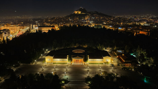 Aerial drone night shot of iconic illuminated public Zappeio hall used for events and lycabettus hill at the background , Athens historic centre, Attica, Greece