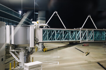 Naklejka premium Airport jet bridge at night. Passenger boarding bridge connected to terminal. Modern airport infrastructure on empty apron. Air travel logistics scene. Industrial transport architecture.