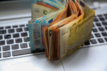 A stack of Euro banknotes of varying denominations, 200 and 50, piled on top of a laptop. Digital economy concept