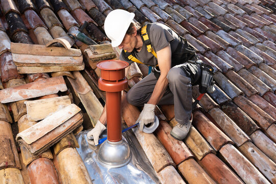 Roofer Installing Chimney on Residential Roof, applying waterproof sealing tape around Vertical Coaxial Boiler Flue