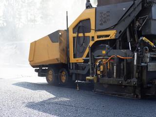 Obraz premium Road paving and asphalt laying. Asphalt paver spreads hot asphalt mixture on the roadway, forming a new road surface during urban infrastructure construction.
