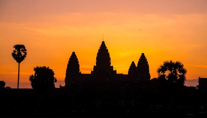 Naklejka premium Silhouetted ancient structure stands against a vibrant orange-hued sunset sky with trees framing the scene