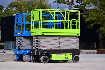 Naklejka premium Modern electric scissor lift parked outdoors on concrete surface. Mobile aerial work platform used for construction, maintenance, warehouse and industrial tasks. Elevated platform with safety rails.