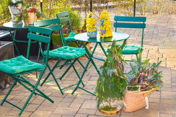 An outdoor seating area with green chairs and tables. A small decorative Christmas tree and basket.