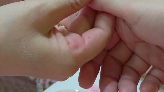 A professional nail technician uses a high-speed electric drill with a gold-toned bit to precisely shape nails during a manicure.