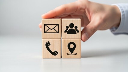 Hand arranges wooden blocks with contact icons on white surface.
