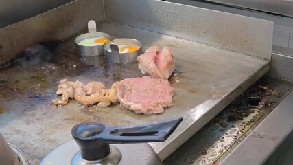 Meat patties and eggs in circular molds cooking on a professional flat-top griddle, ideal for themes of breakfast service or street food preparation.