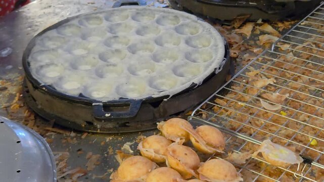 Street vendor cooking Thai coconut pancakes (Khanom Krok) on a cast-iron indented griddle, showcasing traditional street food dessert preparation.