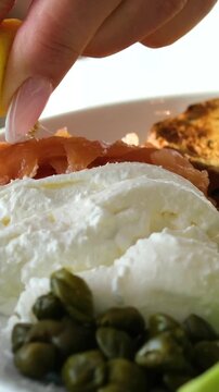squeeze lemon on lightly salted salmon. Plates of mozzarella, peas, beans, spinach, croutons, and berries. Women's hands preparing breakfast.