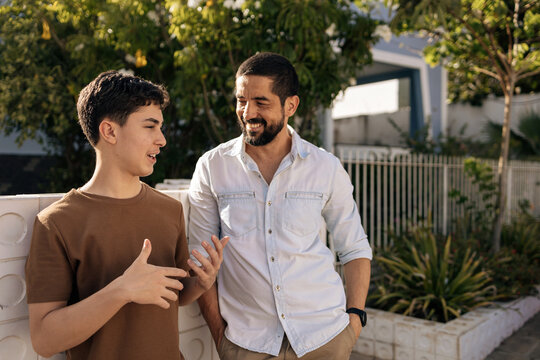 Father and teenage son talk casually outdoors in a residential neighborhood, showing trust, emotional connection, active listening, and a healthy family relationship