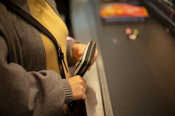 traveler placing wallet into security tray, closeup of hands holding coin purse over conveyor belt, yellow sweater and gray