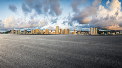 Empty asphalt road and modern city skyline with high-rise buildings under a dramatic sunset sky.