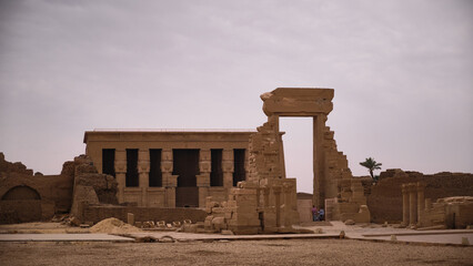 Ancient Egyptian temple ruins with monumental stone gate and massive columns in desert landscape. Weathered sandstone structures and atmosphere of archaeological site. Temple of Hathor, Dendera, Egypt