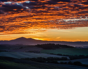 Fototapeta premium Vibrant sunset over rolling hills and distant mountains with colorful cloud formations.