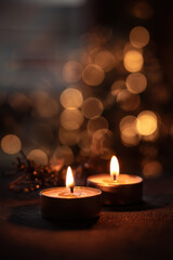 A beautiful and atmospheric close-up of tea light candles glowing warmly in a dark, festive setting. The background is filled with a soft, out-of-focus cascade of golden Christmas lights.