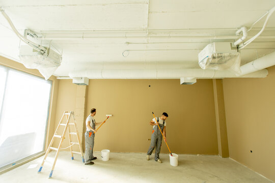 Workers painting an interior wall in a commercial space during daylight hours