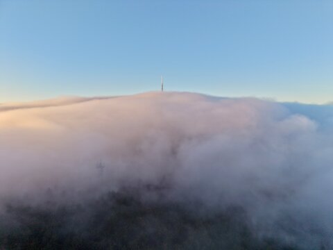 Skyhigh Communication Tower Stands Out Against Thick Cloud Cover Over Wooded Summit At Dawn