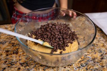 Step-by-step homemade chocolate chip cookie baking process, showing mixing wet and dry ingredients, folding in chocolate chips, and scooping raw cookie dough onto a baking sheet in a home kitchen. 