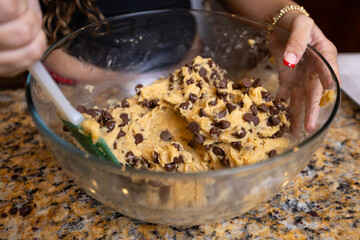 Step-by-step homemade chocolate chip cookie baking process, showing mixing wet and dry ingredients, folding in chocolate chips, and scooping raw cookie dough onto a baking sheet in a home kitchen. 