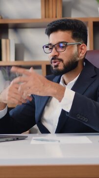 Good-looking indian businessman customer support agent or salesman talking, having virtual meeting working on laptop computer giving online training, remote class on video conference call at modern