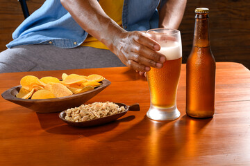 A man's hand reaching out to grab a cold beer and snacks from a wooden table.