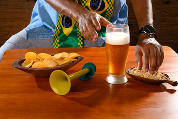A Brazilian fan enjoys beer and snacks while watching a football match.