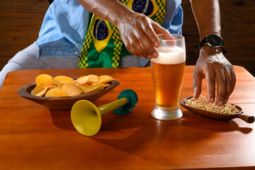 A Brazilian fan enjoys beer and snacks while watching a football match.